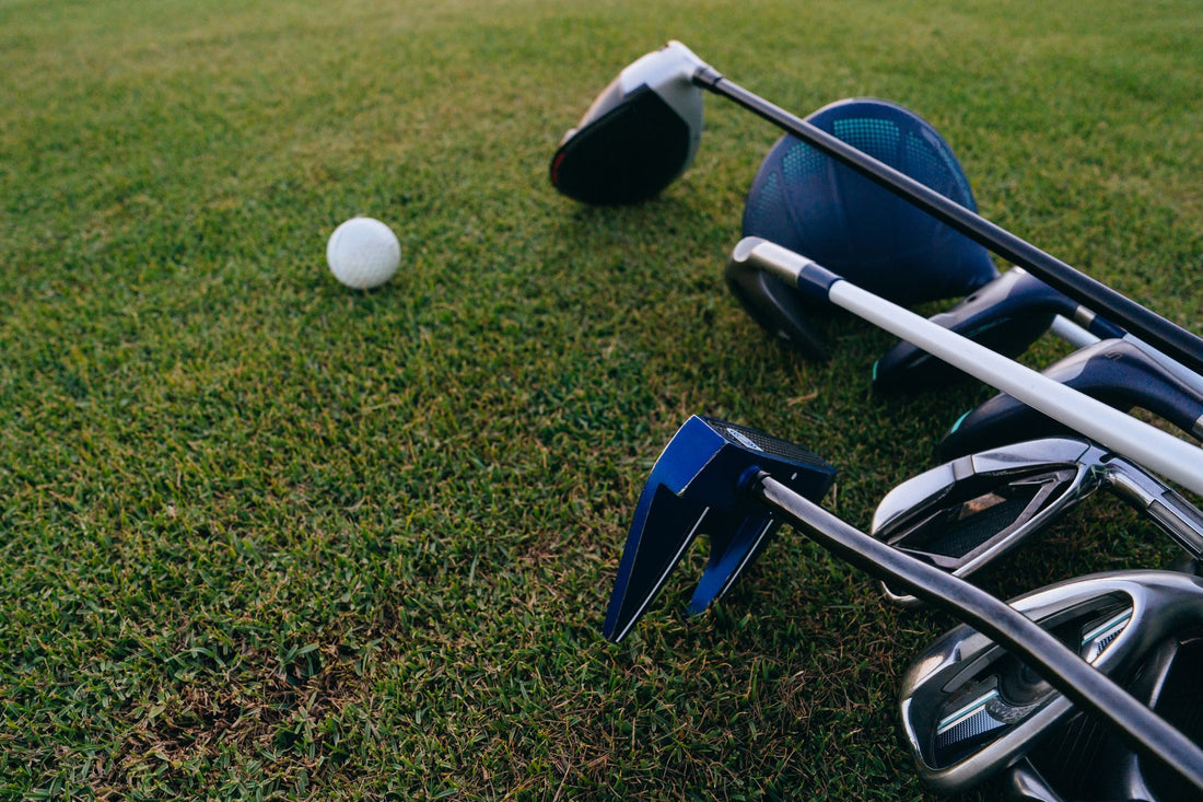 A golf ball sitting on close-cut turf with a driver, irons and a putter laid out beside it