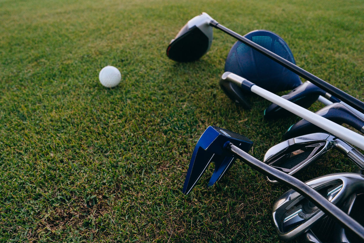 A golf ball sitting on close-cut turf with a driver, irons and a putter laid out beside it